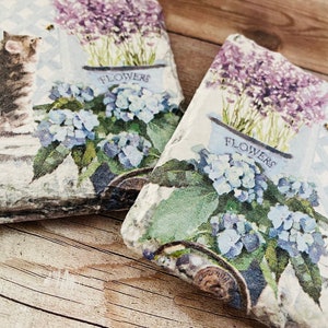 May include: Two decorative stone tiles with a floral and cat design. The tiles feature a watercolor-style print of a kitten, blue hydrangeas, and lavender in a white flower pot. The word "FLOWERS" is printed on the flower pot.