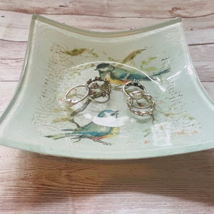 May include: A light blue and white glass dish with a floral design and two birds. The dish has five silver rings inside.