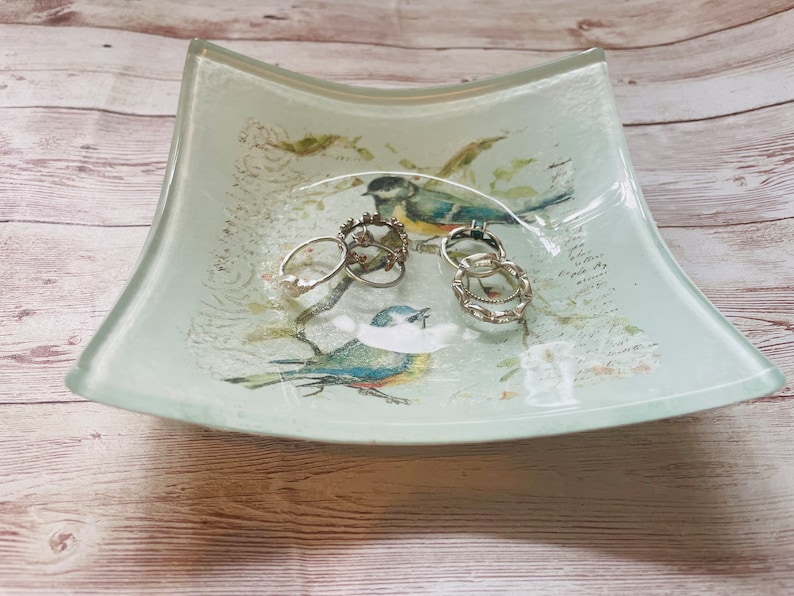 May include: A light blue and white glass dish with a floral design and two birds. The dish has five silver rings inside.