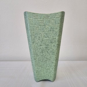 May include: A light green ceramic vase with a woven pattern. The vase has a wide mouth and a narrow base.