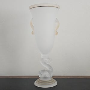 May include: A frosted glass vase with a dolphin base and two curved handles. The vase has a wide top with a gold rim and a slender body. The dolphin is sculpted with detailed fins and a smiling face.