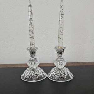 May include: Two clear glass candle holders with a textured design. Each holder has a silver glitter candle inside.
