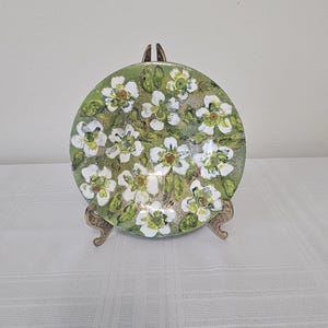May include: A round, green and white ceramic plate with a floral design. The plate is on a gold metal stand.