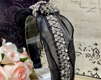 May include: Black headband with a black mesh fabric and a row of rhinestones. The headband is on a white display stand. The text "Aida's Paris" is on a pink and white sign with a black and white polka dot background.