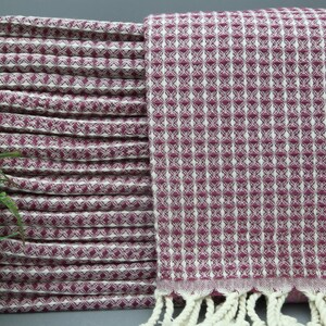 May include: A stack of pink and white patterned Turkish towels with white fringe.