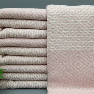 May include: A pink and white patterned throw blanket with a fringe border. The blanket is folded in a stack.