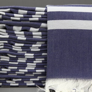 May include: A stack of folded blue and white striped towels with white fringe. The towels are made of a soft, absorbent material.