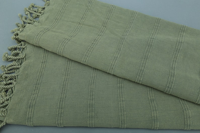 May include: A sage green striped cotton towel with fringed edges.