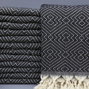 May include: A stack of black and white patterned towels with a geometric design. The towels are folded neatly, showcasing a repeating diamond and zigzag pattern. The edges are finished with a fringe.