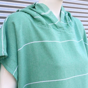 May include: A light green hooded poncho featuring a woven texture and thin horizontal white stripes. The garment has short sleeves and a hood, constructed from a textured fabric with a visible weave pattern, displayed on a white mannequin.