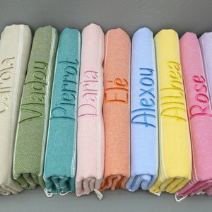 Peut inclure: Dix serviettes colorées avec des noms brodés, dont "Carla", "Ellie", "Alexou", "Althea", "Rose" et "Babou".