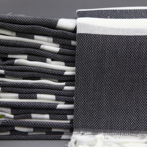 May include: A stack of black and white striped towels with a single towel folded in half on top. The towels have a fringe edge.