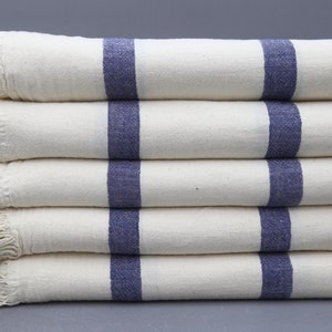 May include: Stack of five white towels with blue stripes. The towels have a fringe border.