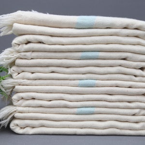 May include: A stack of white towels with a light blue stripe on each towel. The towels are folded and stacked on a gray surface.