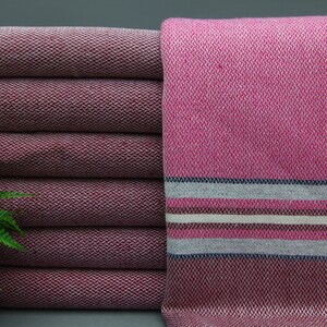 May include: A stack of five burgundy towels with a pink and white striped towel on the right. The towels have a woven texture.