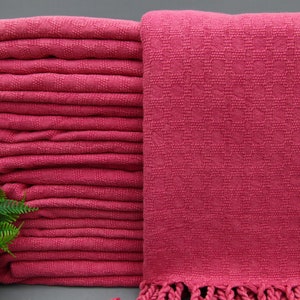 May include: A stack of pink cotton towels with fringed edges. The towels are folded and stacked neatly.