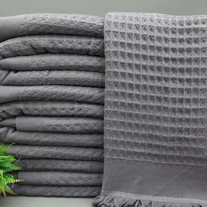 Peut inclure: Une pile de serviettes en tissu gaufré gris avec des bords frangés. Les serviettes sont pliées et empilées proprement.