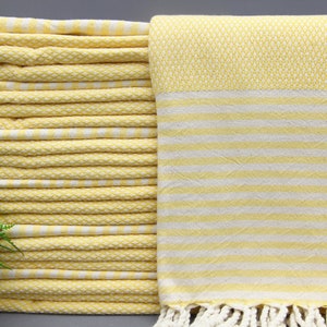 May include: A stack of yellow and white striped Turkish towels with fringe. The towels are folded and stacked on a gray surface.
