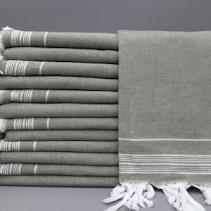 May include: A stack of ten green towels with white stripes and white fringe. The towels are folded and stacked on a gray surface.