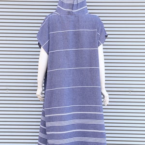 May include: A hooded poncho in a deep blue color featuring thin horizontal white stripes throughout the fabric. The garment has short sleeves, a loose fit, and a bottom hem finished with decorative white fringe tassels along the entire edge.