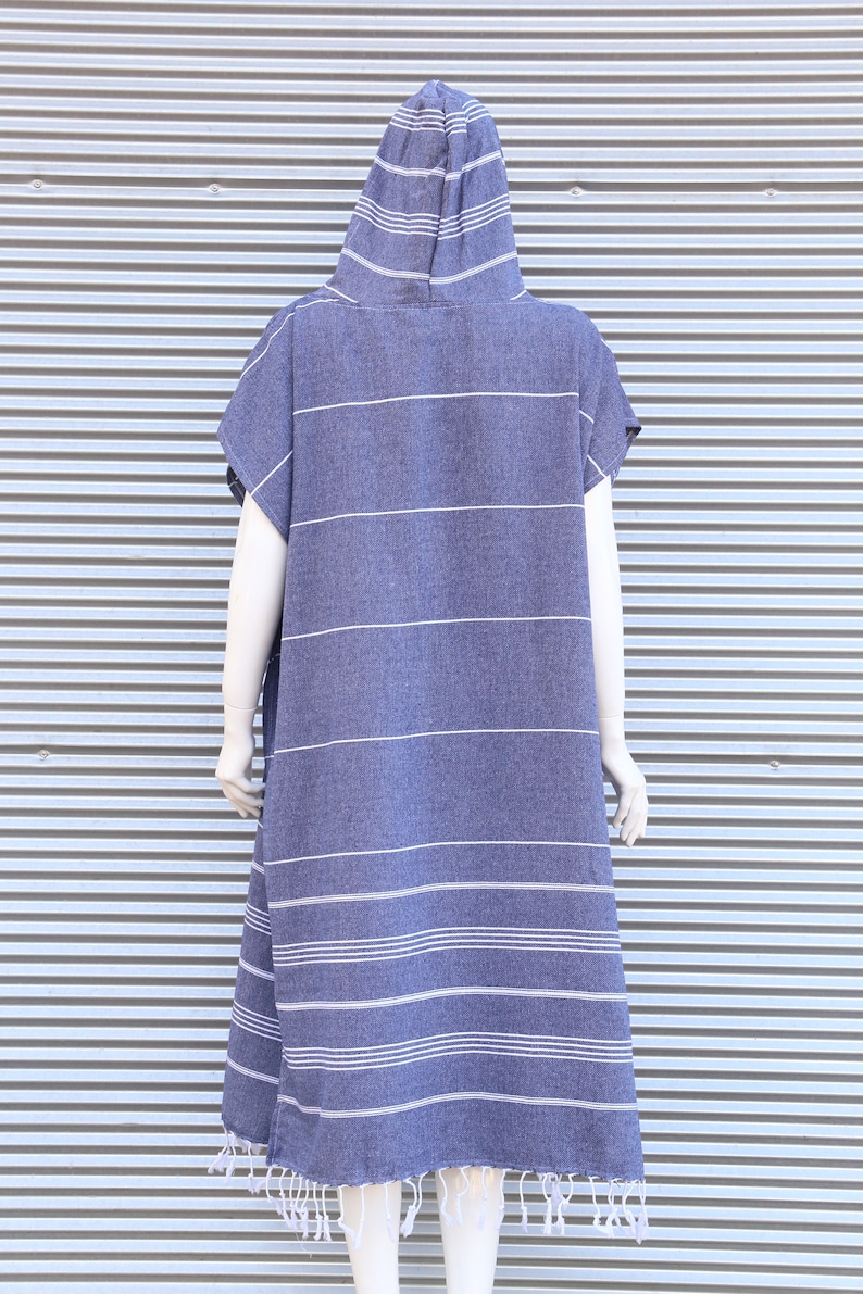 May include: A hooded poncho in a deep blue color featuring thin horizontal white stripes throughout the fabric. The garment has short sleeves, a loose fit, and a bottom hem finished with decorative white fringe tassels along the entire edge.