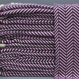 May include: A stack of purple and white striped towels with a herringbone pattern. The towels have a fringe on the ends.