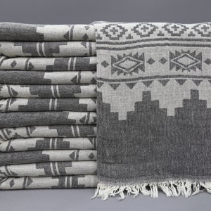 Puede incluir: Una pila de toallas de color gris y blanco con un borde de flecos. Las toallas están dobladas y apiladas sobre una superficie gris.