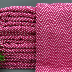 Puede incluir: Una pila de mantas de tiro de color rosa y blanco con estampado de chevron. Las mantas están dobladas y apiladas una encima de la otra.