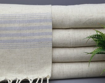 Può includere: Un mucchio di asciugamani color crema con strisce blu. Gli asciugamani hanno una frangia sul bordo inferiore.