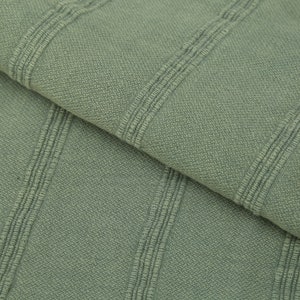 May include: Close-up of a sage green fabric with a ribbed texture. The fabric has vertical stripes that are slightly raised.