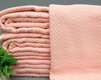 May include: A stack of pink and white striped towels with a chevron pattern. The towels are folded and stacked on a gray surface.