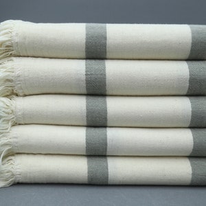May include: A stack of five white towels with gray stripes and fringed edges. The towels are folded and stacked on a gray surface.
