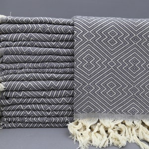 May include: A stack of gray and white patterned Turkish towels with fringe. The towels are folded and stacked on a gray surface.