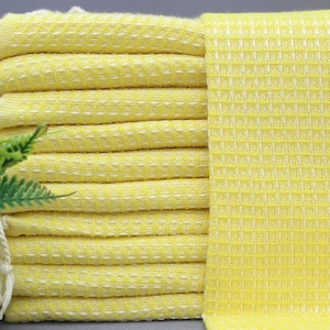 May include: A stack of yellow waffle weave towels with white fringe. The towels are folded and stacked on a gray surface.