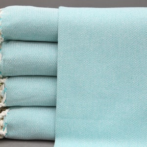 Peut inclure: Pile de quatre serviettes en coton bleu turquoise avec des franges blanches. Les serviettes sont pliées et empilées sur une surface grise.