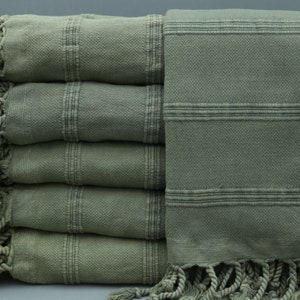 May include: A stack of five green Turkish towels with fringe. The towels have a striped pattern.