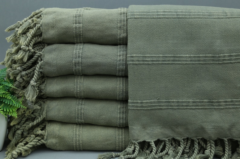 May include: A stack of five green Turkish towels with fringe. The towels have a striped pattern.