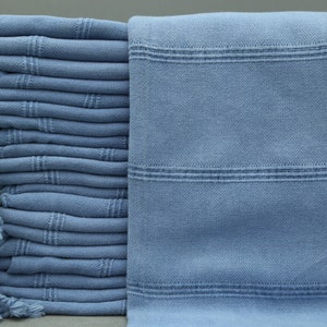 May include: A stack of light blue Turkish towels with fringe edges. The towels are folded and stacked neatly.