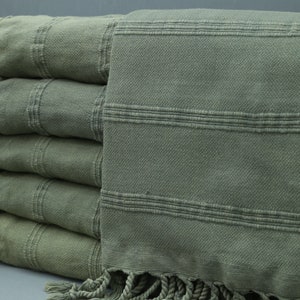 May include: A stack of five green Turkish towels with fringe. The towels are folded and have a striped pattern.