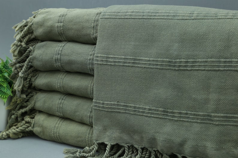 May include: A stack of five green Turkish towels with fringe. The towels are folded and have a striped pattern.