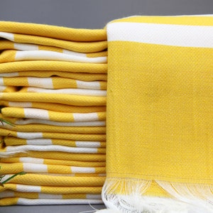 May include: A stack of yellow and white striped towels with a single towel folded in front. The towels have a fringe border.