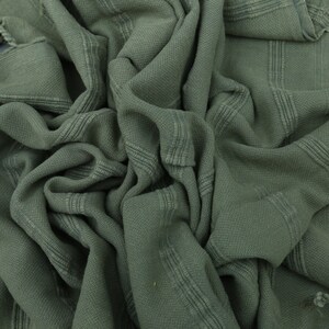 May include: A soft, green, woven cotton towel with fringed edges. The towel is folded and textured.