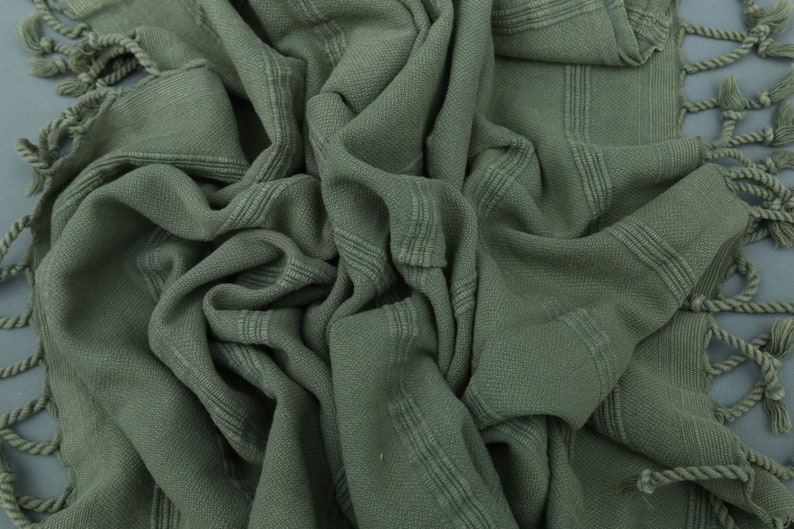 May include: A soft, green, woven cotton towel with fringed edges. The towel is folded and textured.