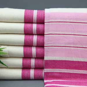 May include: A stack of white towels with pink stripes. The towels are folded and have a fringe on one end.