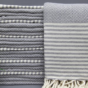 May include: A stack of gray and white striped Turkish towels with fringe. The towels are folded and stacked on top of each other.