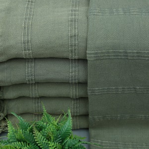 May include: A stack of green Turkish towels with fringed edges. The towels are made of cotton and have a soft, absorbent texture.