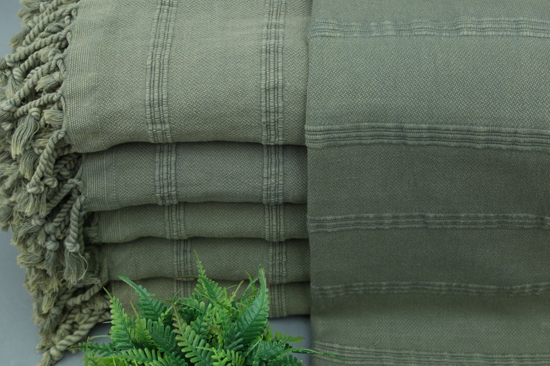 May include: A stack of green Turkish towels with fringed edges. The towels are made of cotton and have a soft, absorbent texture.