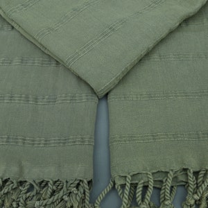 May include: A pair of green Turkish towels with fringe. The towels are made of cotton and have a woven texture.