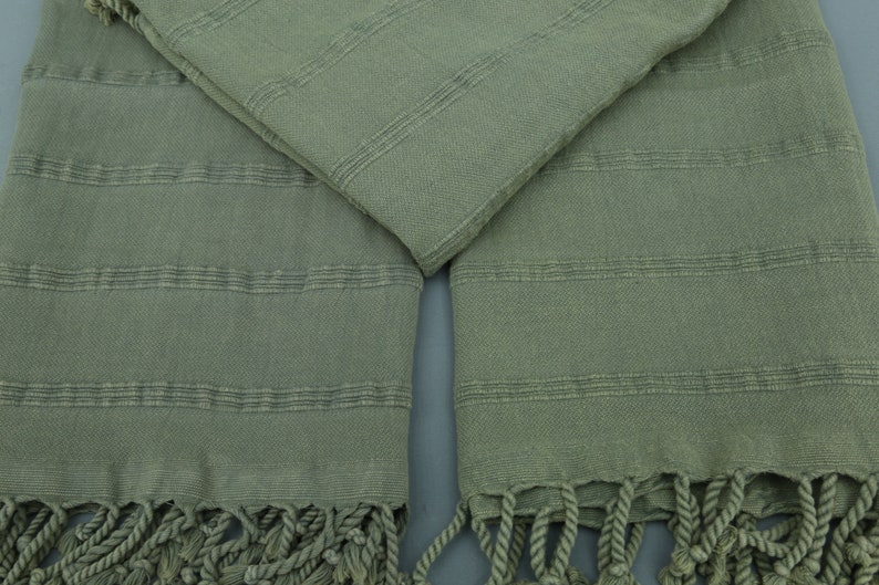 May include: A pair of green Turkish towels with fringe. The towels are made of cotton and have a woven texture.