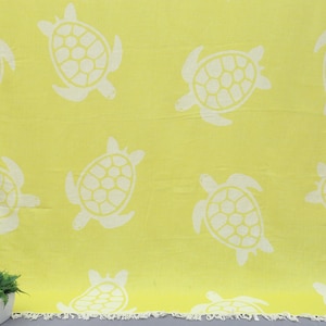 Op de afbeelding: Een gele strandhanddoek met een wit schildpadpatroon. De handdoek heeft een gefranst randje.